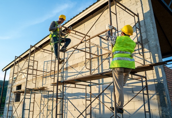 Construction workers in uniform and safety equipment working on scaffolding at building site.