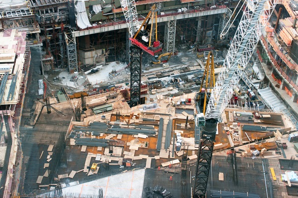 An overhead view of a large, complex New York City construction site featuring multiple cranes, scaffolding, and various building materials.